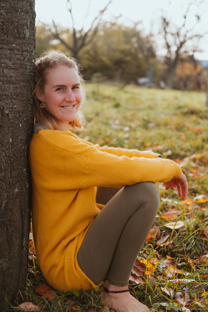 Unternehmerin in gelbem Pullover lehnt lächelnd an einem Baum – Business-Portrait Darmstadt
