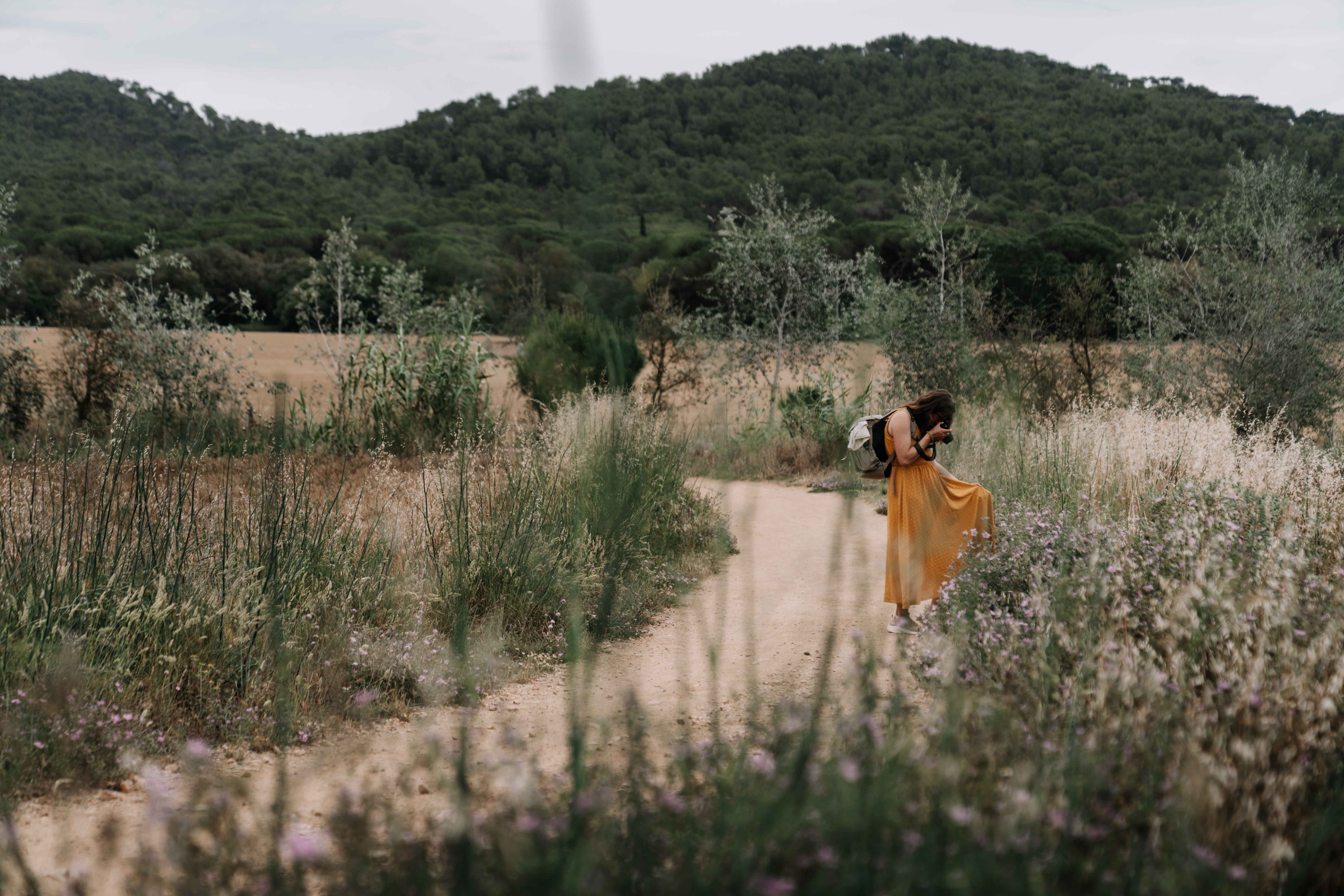Mareen Zimmermann fotografiert auf einem Feldweg beim Inspiralab Retreat in Spanien, gelbes Kleid, Wildblumen