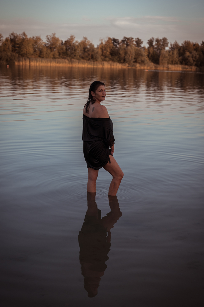 Frau steht im See im schwarzen Kleid und blickt über die Schulter, warmes Abendlicht – Seelenfotografie von MALEA Fotografie